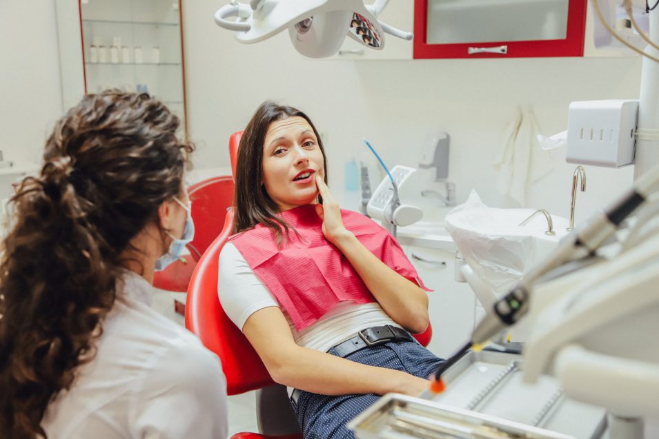 Close-up portrait of a sad young girl with a painful tooth, a doctor in office chairs, an isolated dentist office background clinic.