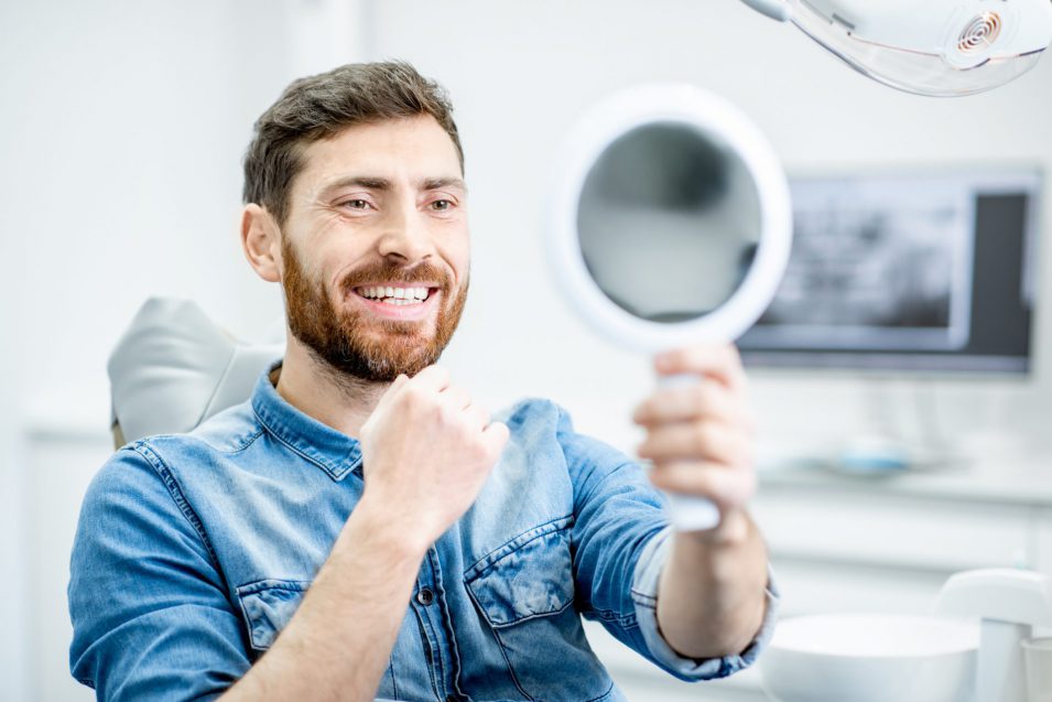 Young man checking teeth after receiving dental crown placement from cosmetic dentist