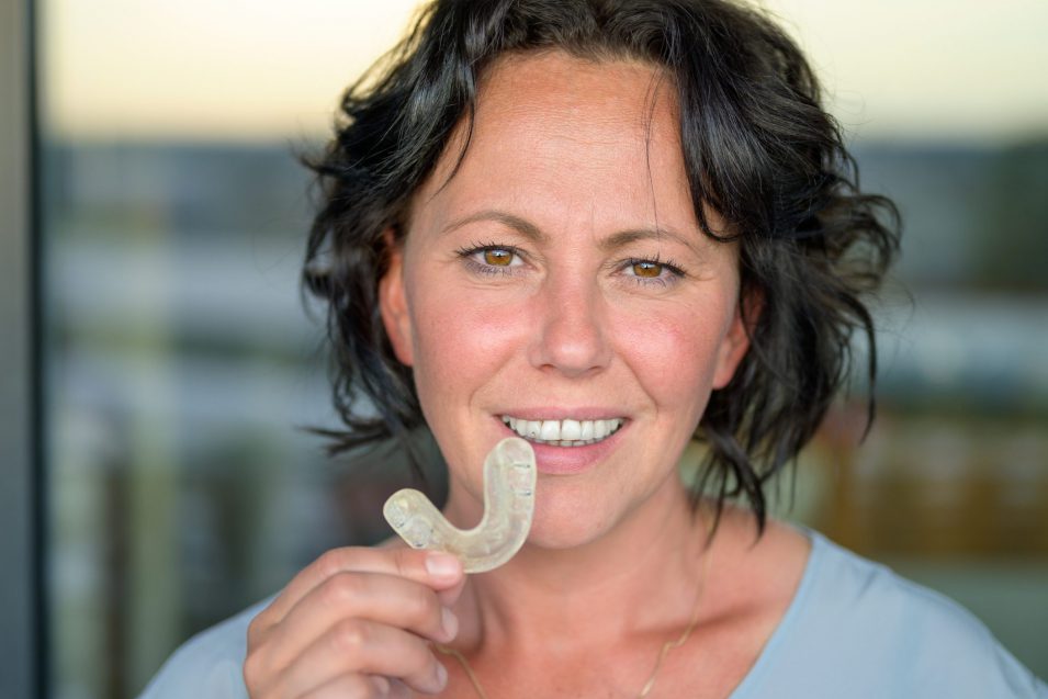 a smiling woman holding a mouth dental guard in Brantford