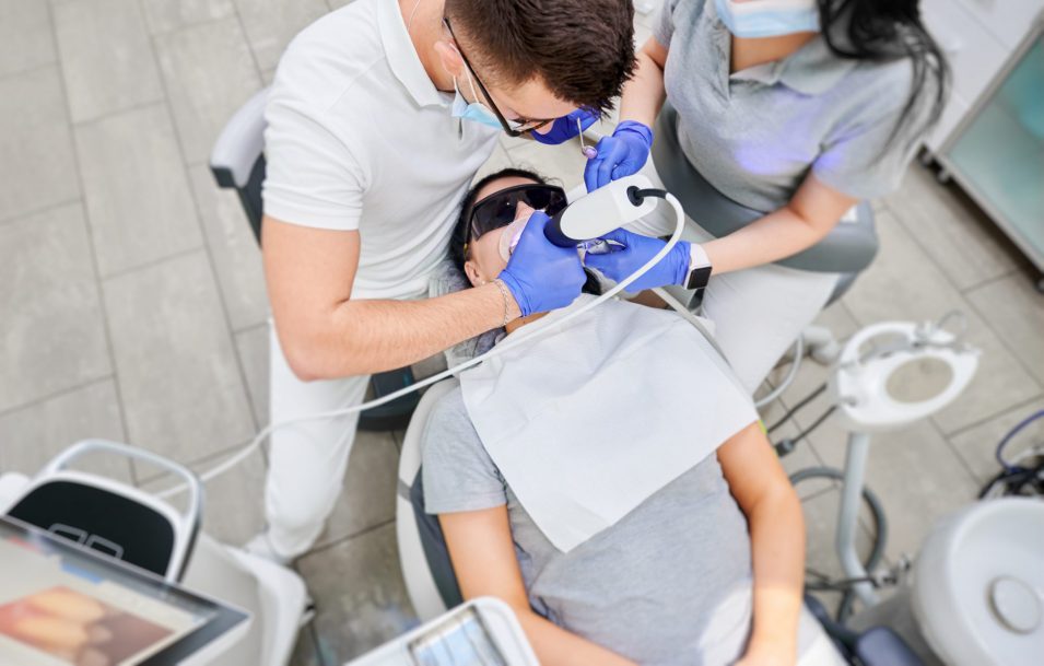 Doctor and assistant examining patient teeth with intraoral scanner.